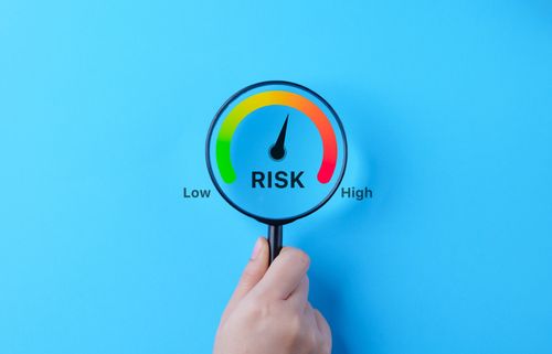 Business Risk Gauge with Low to High Indicator. A hand holding magnifying glass over a risk gauge, showing a scale from low to high, symbolizing the concept of business risk assessment and management.